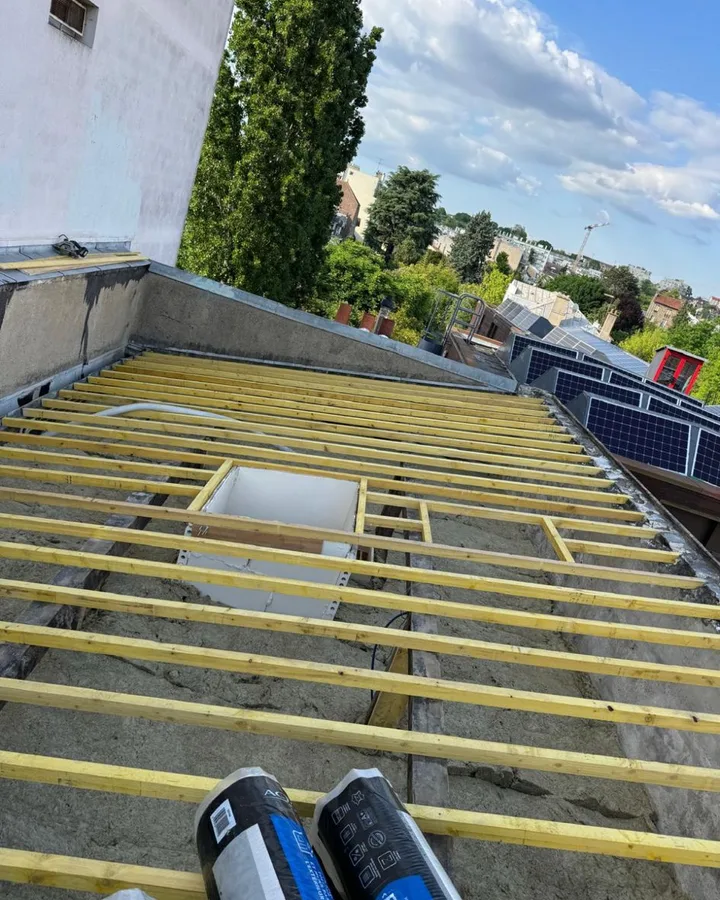 Chevronnage neuf en bois clair posé sur toute la longueur d'un versant, deux rouleaux de membrane d'étanchéité prêts à dérouler.