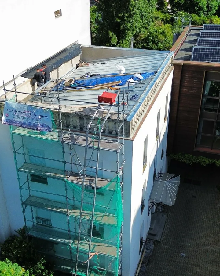 Chantier de couverture sur un immeuble : échafaudage monté en façade, filet de chantier vert, zone de travail bâchée sur le toit.