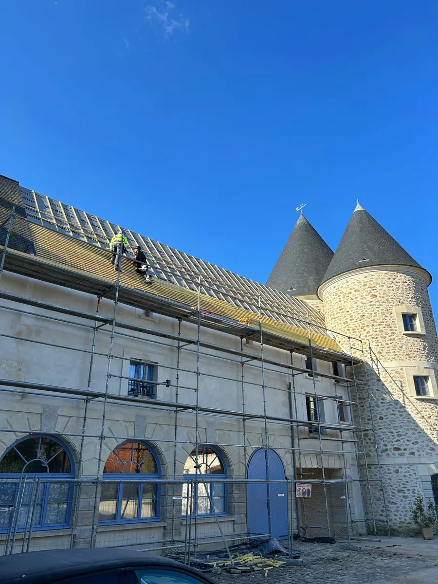 Chantier de couverture sur un bâtiment ancien flanqué de deux tours en poivrière : écran sous-toiture déroulé et liteaunage neuf posé sur tout le versant, deux couvreurs au travail, échafaudage de pied monté sur toute la façade.